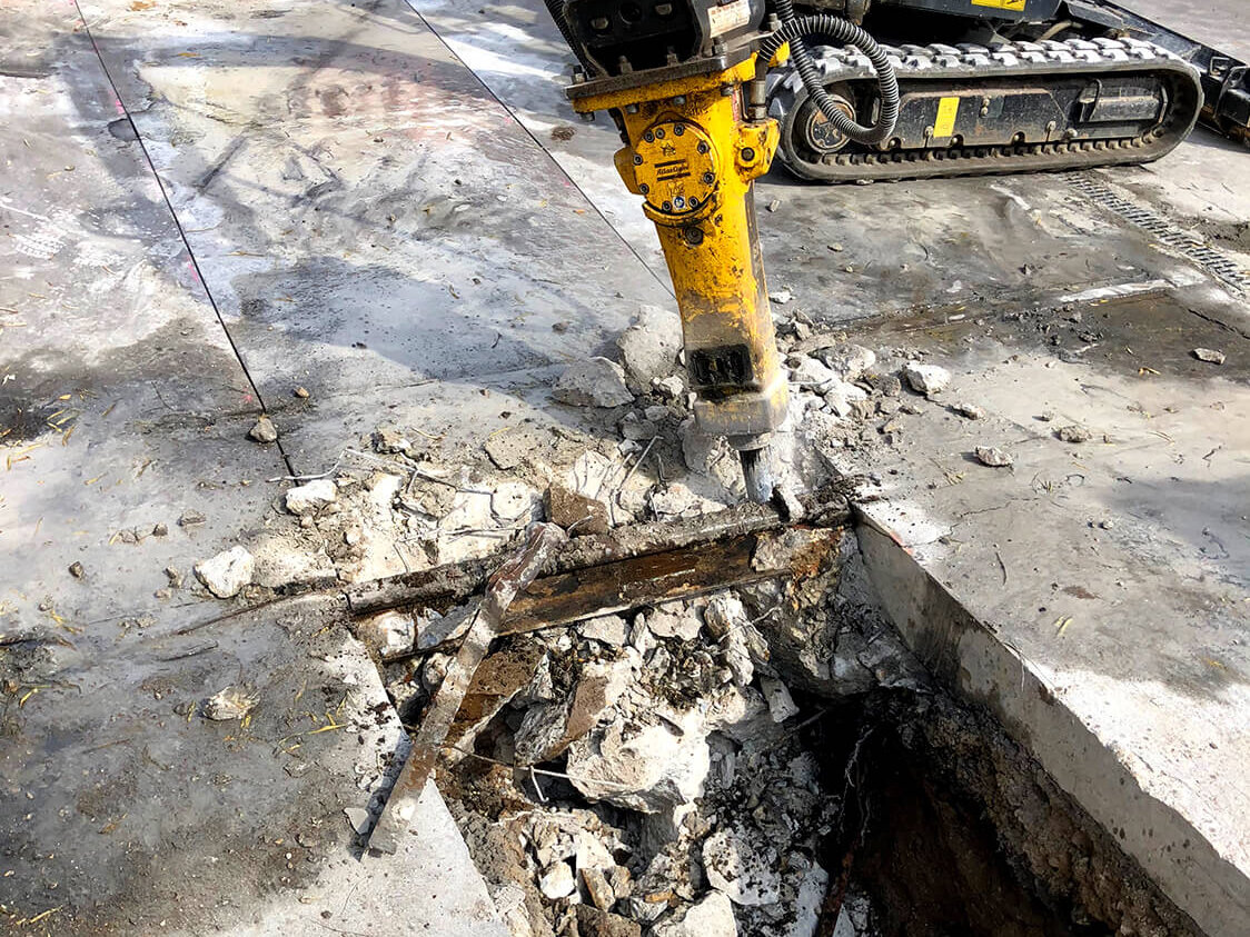 Mini-Bagger und Presslufthammer beim Öffnen einer Asphaltdecke