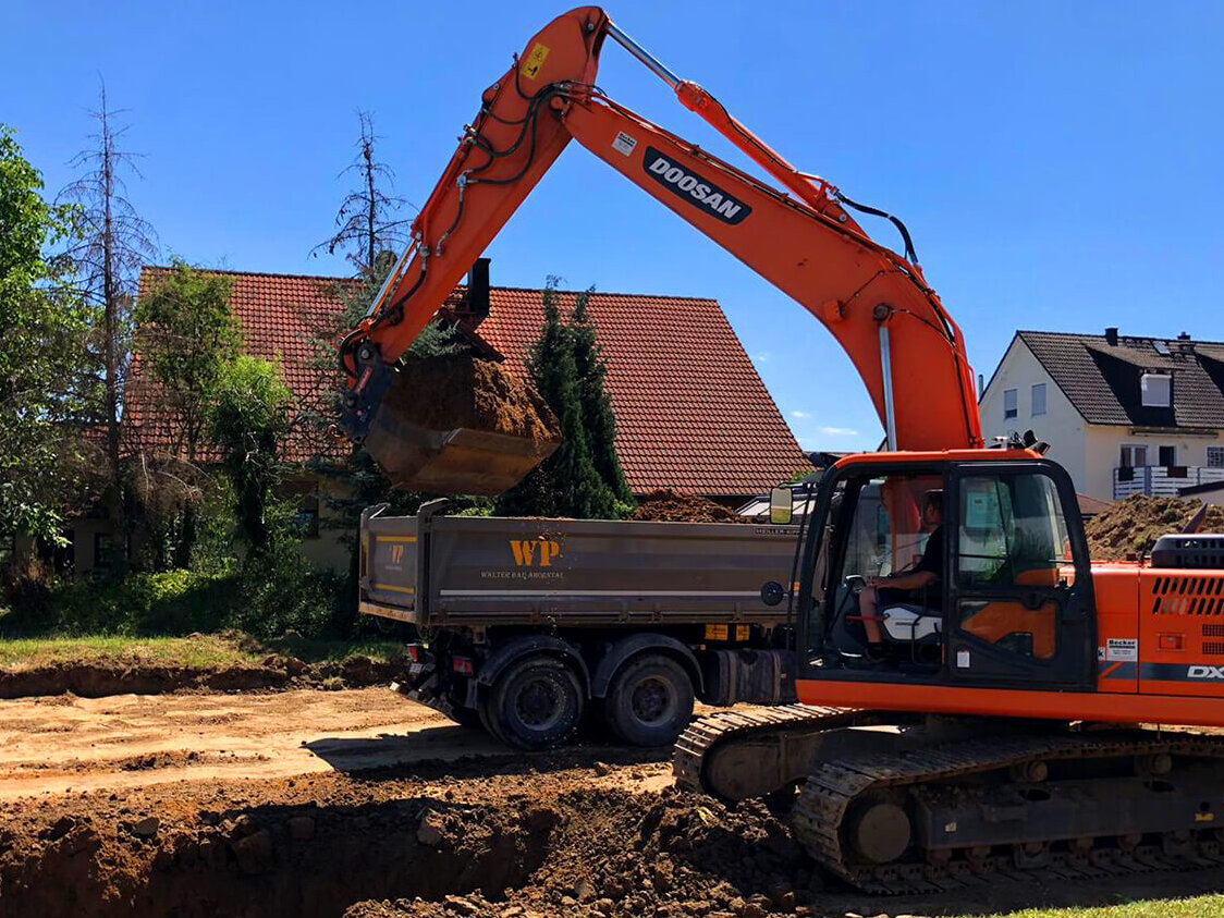 Kettenbagger baggert Kanal für Anschlüsse, LKW transportiert Erdaushub ab